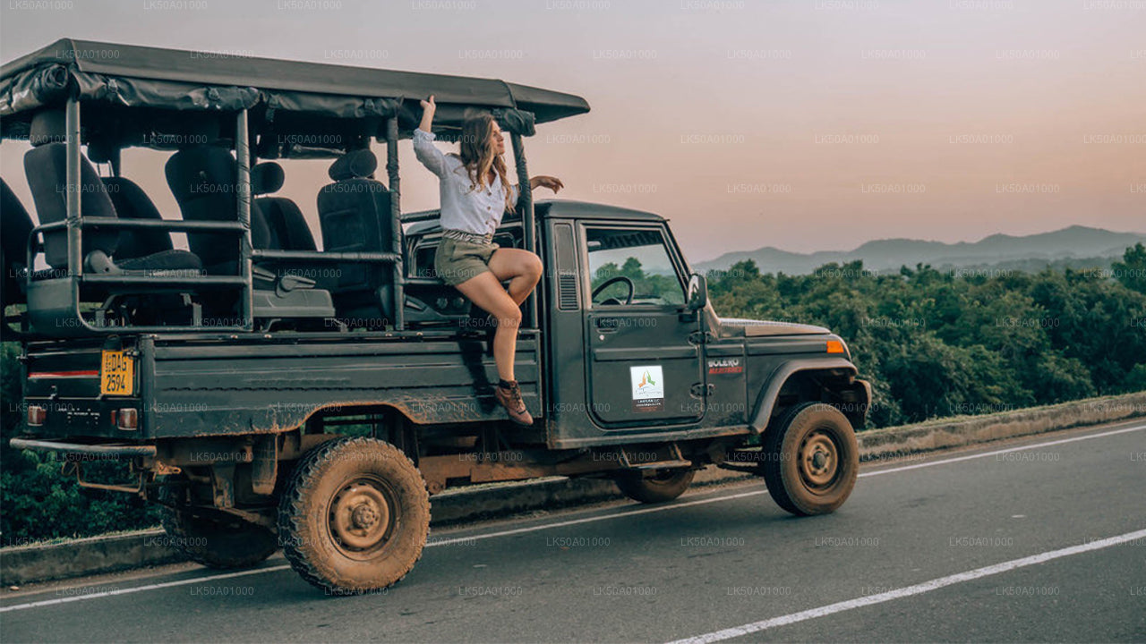 A person sitting on the edge of a moving safari jeep, with a scenic view of Udawalawe National Park.